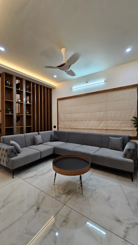 Grey L-shaped sofa facing a fabric-panelled wall under a cove-lit ceiling