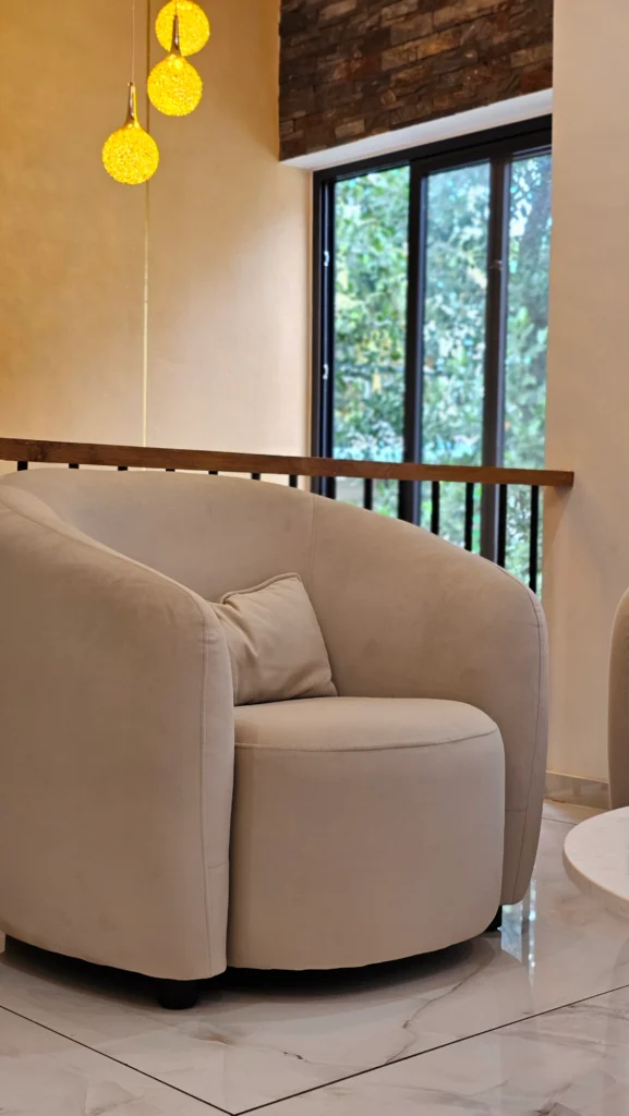 Curved beige armchair beside a stairwell with pendant lights