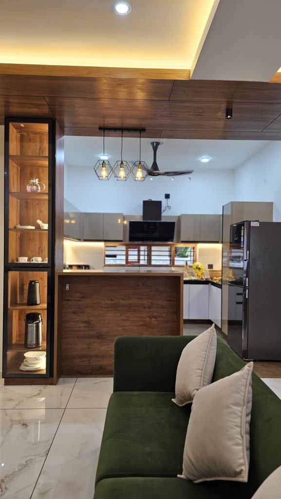 A green sofa and timber display partition opening onto a fitted kitchen