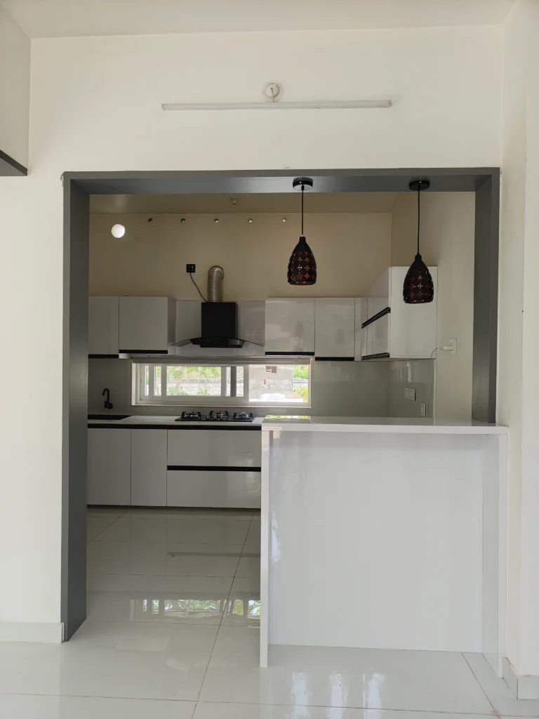 White modular kitchen with a breakfast counter and pendant lights