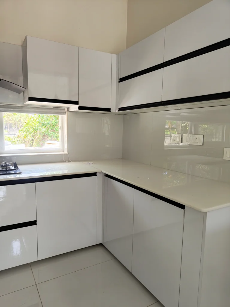 White modular L-shaped kitchen with high-gloss cabinets and black handle profiles