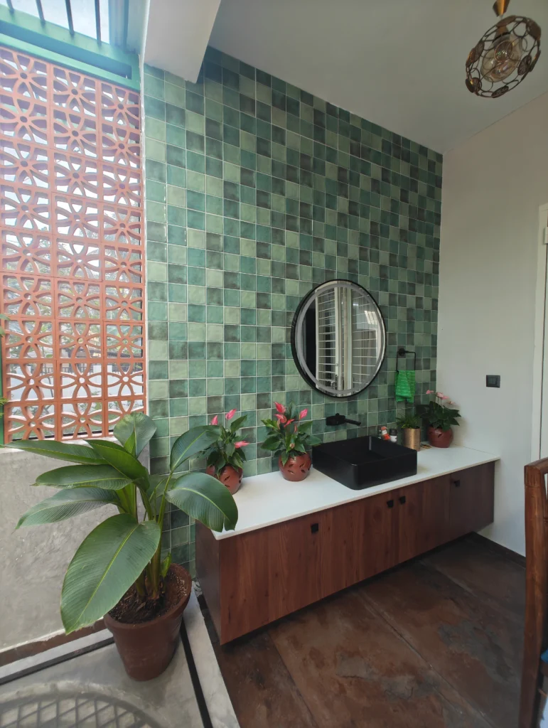 Green tiled wall with a round mirror, timber console and a terracotta jaali screen