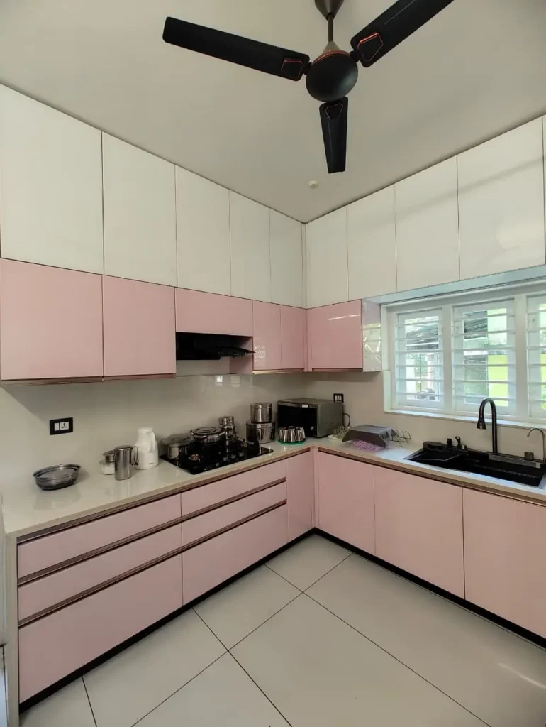 Pastel pink U-shaped kitchen with white wall cabinets and a black sink