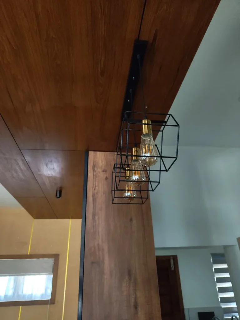 Black wire cube pendant lights with filament bulbs under a timber ceiling