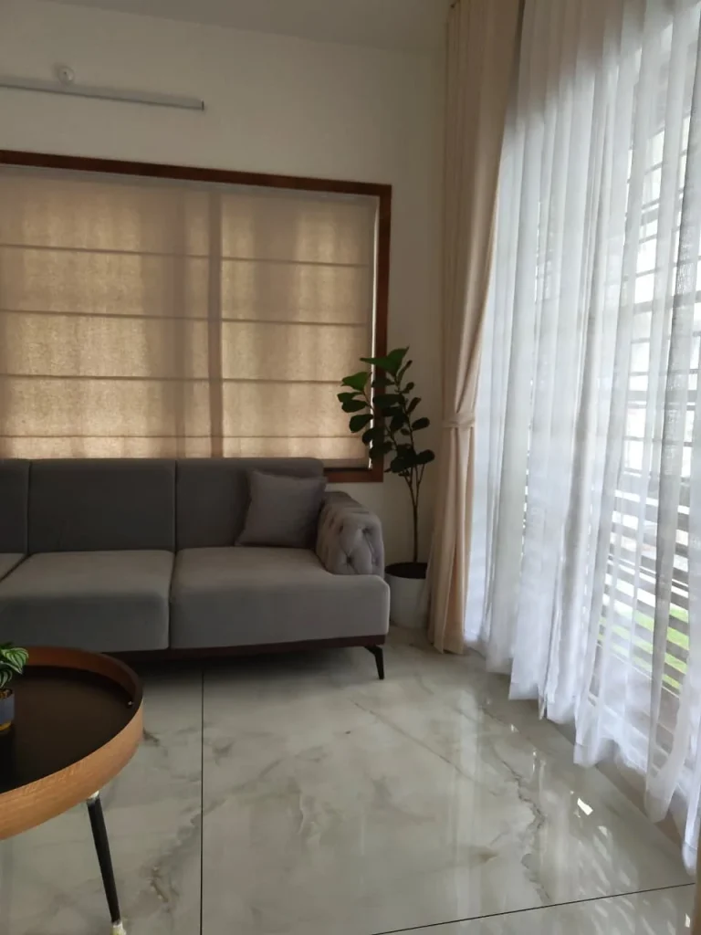 Grey sofa beside a Roman blind and sheer curtains on a marble floor